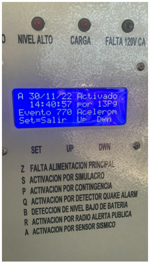 Pantalla LCD azul de Alarma Sísmica SIDESICCO V6 mostrando activación por acelerómetro e indicadores LED de carga.